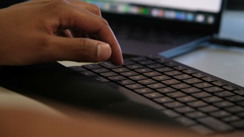 Close up of a hand typing on a laptop keyboard with a colorful screen blurred in the background