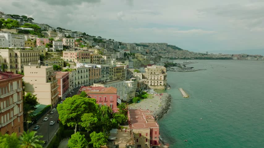Aerial drone video of the Gulf of Naples, Italy, showing the coastal waterfront, boats, blue sea, shoreline, and surrounding landscape. A natural Mediterranean scene capturing the calm water and scenic Naples coastline.