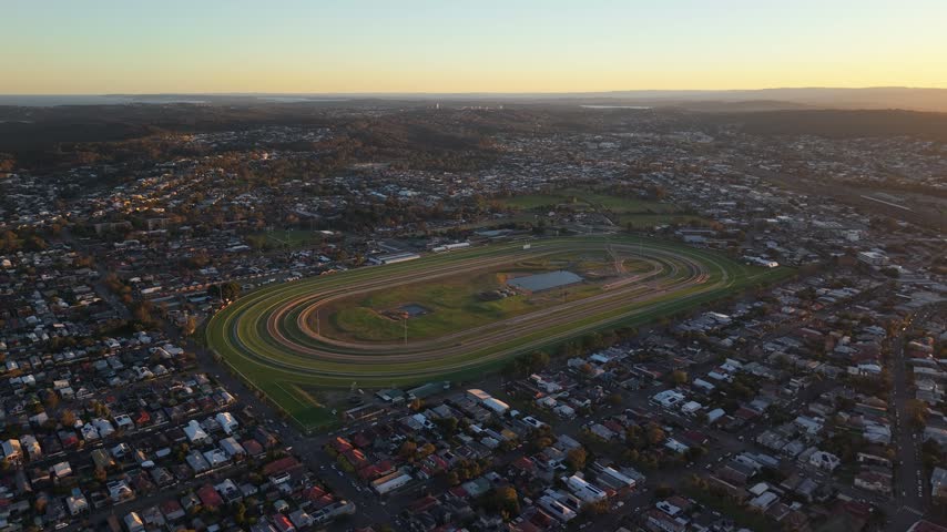 Newcastle Racecourse amid expansive residential suburbs under warm sunset light, aerial panoramic dolly