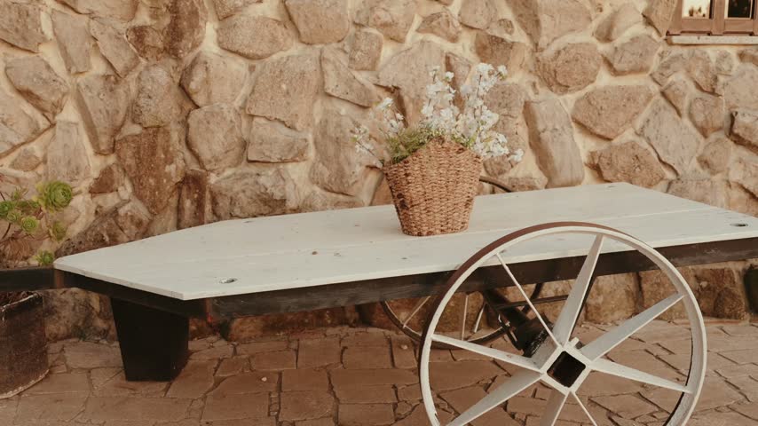 White wooden cart table with a flower basket against a rustic stone wall