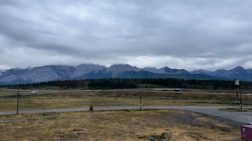Wide view of Alberta prairie with distant mountains under cloudy sky, rural roadside