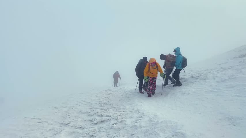 Tourist group ascending uphill on Mount Ararat during storm wind and snow, showing guided summit push, extreme weather trekking, teamwork, endurance, and alpine expedition challenge