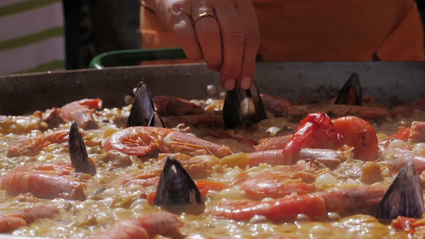 Chef Cooking traditional Spanish Paella on a stove, food festival in barcelona spain. Chef cooking food on fire from mussels, shrimp, squid rice, Catalan catalonian cuisine, street food truck.