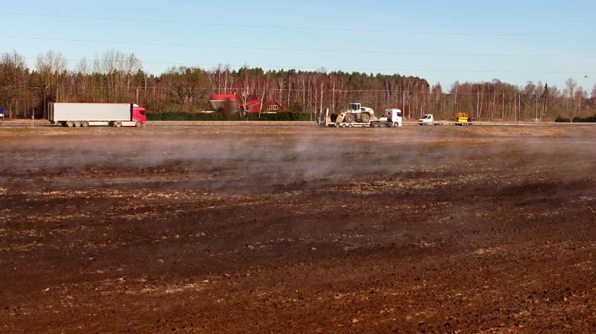 Low mist drifts over spring farmland as trucks and farm vehicles travel highway