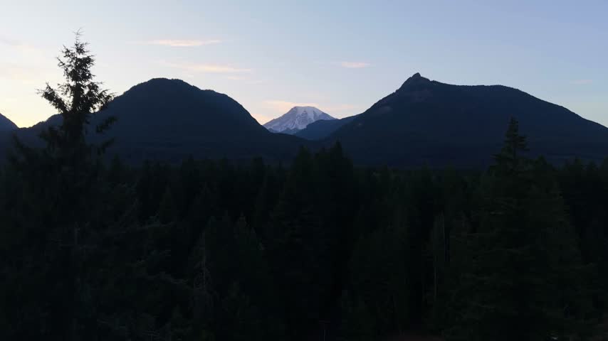 Aerial footage of Mount Rainier visible beyond forested mountain ridges near Packwood, Washington, during a peaceful summer evening.
