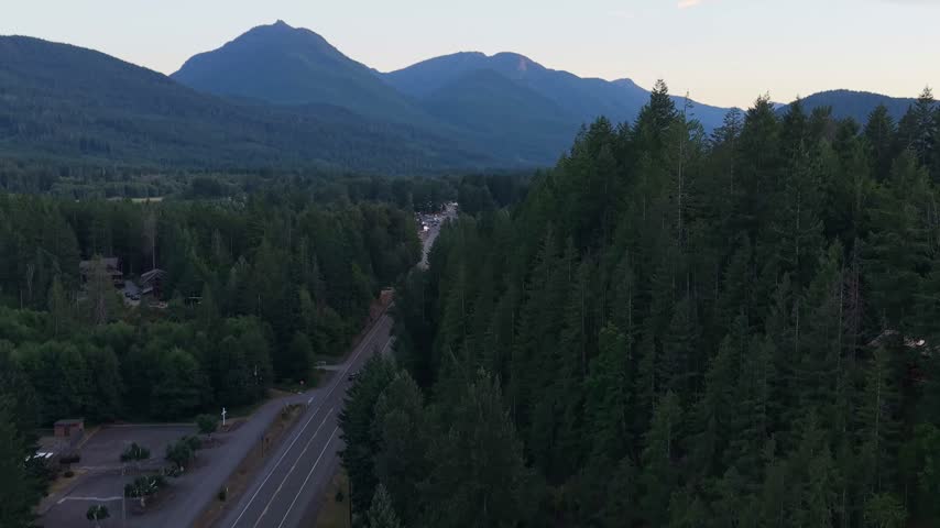 Aerial view over the forested landscape near Packwood, Washington, with a mountain range in the distance and a rural road winding through the trees during evening light.
