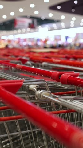 Close-up of empty metal shopping carts with red handles nested together in a row inside a large modern supermarket or hypermarket. Retail trade, consumerism, and shopping concept.