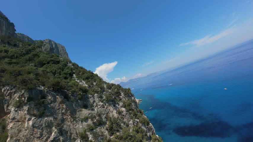 Sheer limestone cliffs drop into deep blue water along Golfo di Orosei, Sardinia — FPV drone flying low along the rugged Mediterranean coastline, Italy.