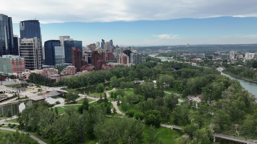 panning left along Skyline of Downtown Calgary ( Alberta, Canada)  to Centre St Bridge, with Prince’s Island Park and Bow River below and skyscrapers in front - 4k aerial video footage 