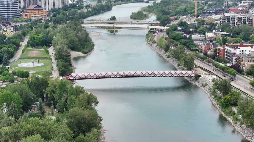 flying above Bow River next to Prince’s Island Park towards Peace Bridge and Bow River Pathway, with parts of Downtown Calgary ( Alberta, Canada) on left side - 4k aerial video footage 