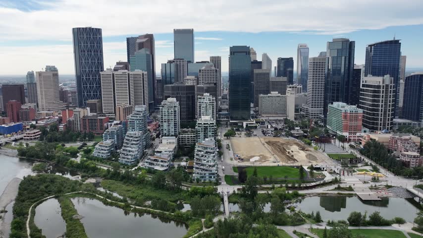 flying along Skyline of Downtown Calgary ( Alberta, Canada) and panning left  to Centre St Bridge, with Prince’s Island Park and Bow River below - 4k aerial video footage 