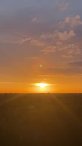 Vertical tripod timelapse of vivid orange sunset with sun going down over Florida skyline and soft clouds.