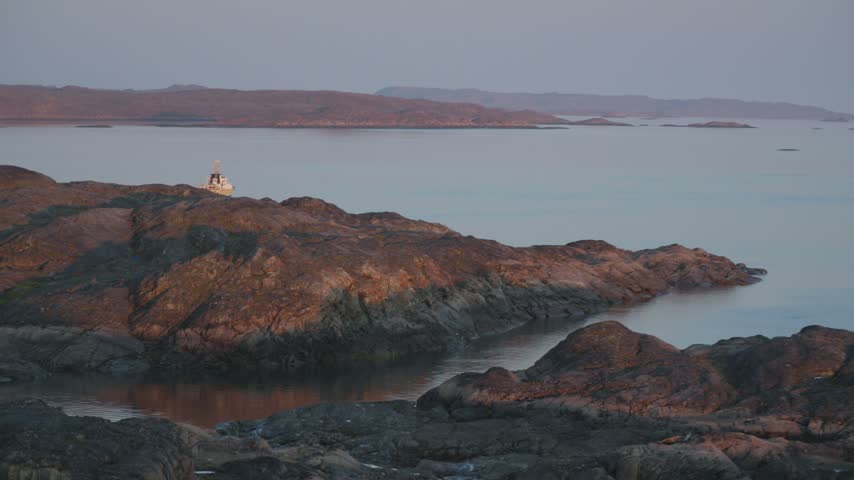 Wide landscape shot showing the research vessel Coriolis II steaming out of the bay past rocky coastal points under warm golden sunset light.