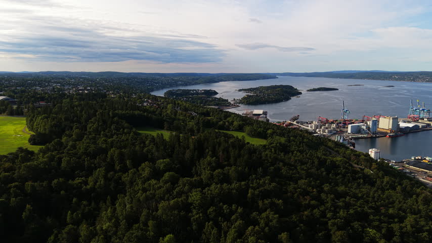 Dense green hills, bright meadow clearings and Oslo’s container port stretch toward the Oslofjord under soft daylight.