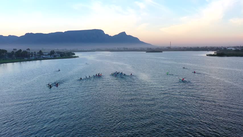 Aerial view of people kayaking on a lake with Table Mountain in the background during golden hour in Cape Town, Western Cape, South Africa.