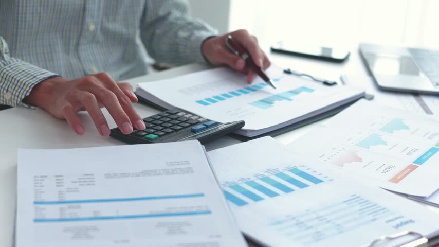 Businessman working at office desk using calculator analyzing financial charts data in office.