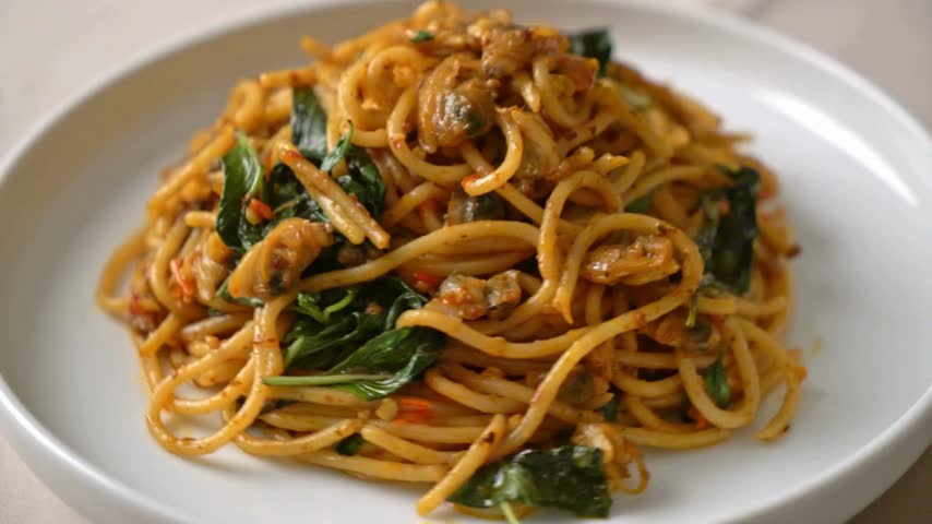 Close up rotating view of stir fried pasta with clams chili paste and basil in slow motion video clip.