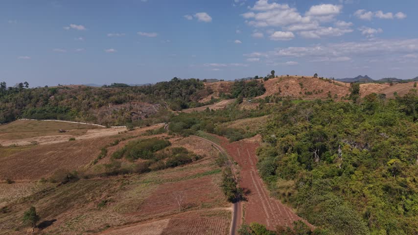 Aerial view of a dirt road cutting through banana plantation and farmland with misty mountains in the background.