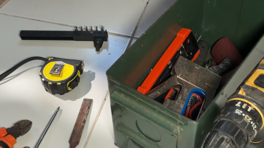 Overhead shot of a collection of working tools including an adjustable wrench, tape measure, pliers, screwdriver, and metal file arranged on a white tile floor. A hand is seen picking up the adjustable wrench and retracting the measuring tape. Useful for construction, DIY, maintenance, and workshop concepts