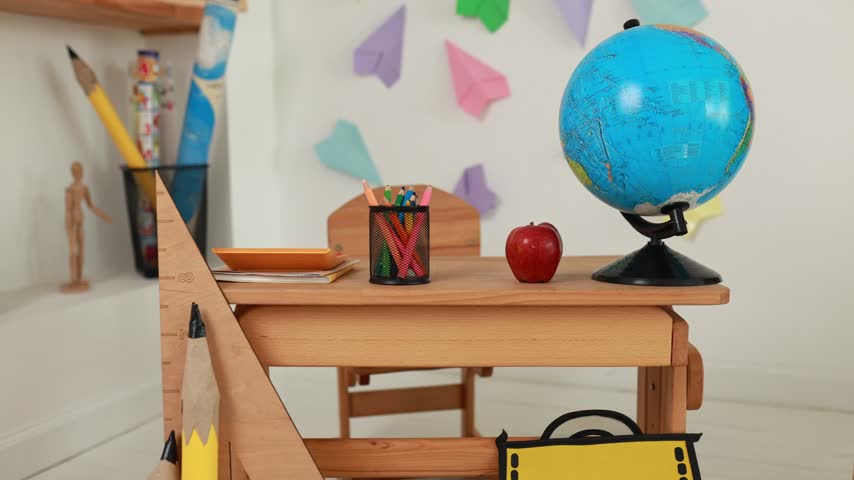 Empty wooden study desk decorated for primary education with globe, apple, and stationary set. Back to school lifestyle concept, colorful paper airplanes decor, learning background, and copy space.