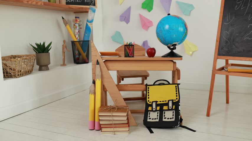 Empty primary interior school classroom setup with wooden desk, globe, apple, chalk board easel. Back to school concept, colorful paper airplanes wall decor, study background, and school supplies.