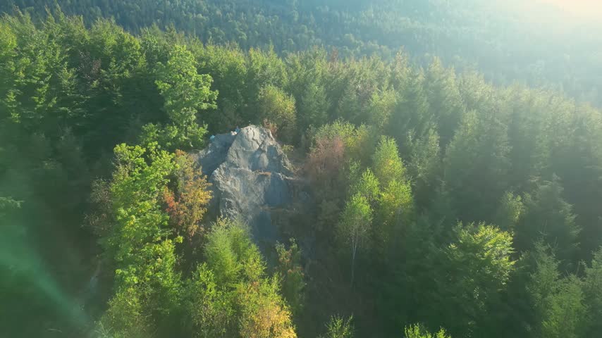 Aerial flyover of a rocky outcrop emerging from misty autumn forest in the Izera Mountains, Poland, Świeradów-Zdrój