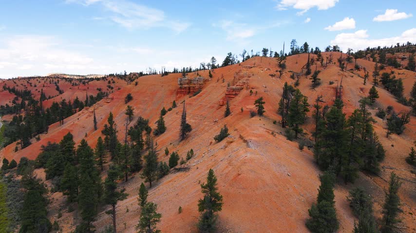 Aerial view of Red Canyon Arch along scenic Utah Route 12, where the highway passes beneath two consecutive natural stone arches carved into vivid red rock pillars near Bryce Canyon National Park. This aerial drone video captures cars gliding through the narrow boulder tunnels, framed by towering hoodoos and pine forest on both sides of the winding mountain road.
The footage reveals the striking color contrast between the rusty red sandstone formations, green ponderosa pine trees and clear blue sky above southern Utah. Carved naturally over centuries by erosion, these twin stone arches form one of the most photographed roadside landmarks along the entire Utah Scenic Byway 12, a route often ranked among the most beautiful drives in the country.
Shot from above, the drone clip follows the curve of the highway as it climbs through Dixie National Forest, revealing layers of eroded stone walls, narrow canyons and dramatic spires rising beside the winding pavement below. Passing vehicles appear tiny beneath the massive boulder gateway, highlighting the scale of this unique geological wonder found nowhere else along the road system of the American West, where nature itself shaped a passage for traffic through solid rock.
Perfect for travel documentaries, tourism marketing, adventure vlogs, road trip content and cinematic projects celebrating the natural beauty of southern Utah. This clip suits stories about scenic drives, national park journeys, exploration, wanderlust and iconic filming locations connecting Bryce Canyon, Zion and the wider Colorado Plateau region, appealing equally to travel brands, bloggers and independent filmmakers.
Whether for a tourism campaign, a documentary intro or a personal passion project, the aerial shot delivers a powerful, high quality visual of a rare natural arch crossing a public highway, capturing the timeless charm of red rock country and the unforgettable drive through ruby Canyon from a bird