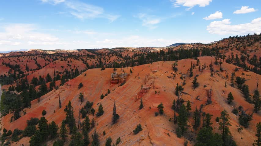 Aerial view of Red Canyon Arch along scenic Utah Route 12, where the highway passes beneath two consecutive natural stone arches carved into vivid red rock pillars near Bryce Canyon National Park. This aerial drone video captures cars gliding through the narrow boulder tunnels, framed by towering hoodoos and pine forest on both sides of the winding mountain road.
The footage reveals the striking color contrast between the rusty red sandstone formations, green ponderosa pine trees and clear blue sky above southern Utah. Carved naturally over centuries by erosion, these twin stone arches form one of the most photographed roadside landmarks along the entire Utah Scenic Byway 12, a route often ranked among the most beautiful drives in the country.
Shot from above, the drone clip follows the curve of the highway as it climbs through Dixie National Forest, revealing layers of eroded stone walls, narrow canyons and dramatic spires rising beside the winding pavement below. Passing vehicles appear tiny beneath the massive boulder gateway, highlighting the scale of this unique geological wonder found nowhere else along the road system of the American West, where nature itself shaped a passage for traffic through solid rock.
Perfect for travel documentaries, tourism marketing, adventure vlogs, road trip content and cinematic projects celebrating the natural beauty of southern Utah. This clip suits stories about scenic drives, national park journeys, exploration, wanderlust and iconic filming locations connecting Bryce Canyon, Zion and the wider Colorado Plateau region, appealing equally to travel brands, bloggers and independent filmmakers.
Whether for a tourism campaign, a documentary intro or a personal passion project, the aerial shot delivers a powerful, high quality visual of a rare natural arch crossing a public highway, capturing the timeless charm of red rock country and the unforgettable drive through ruby Canyon from a bird