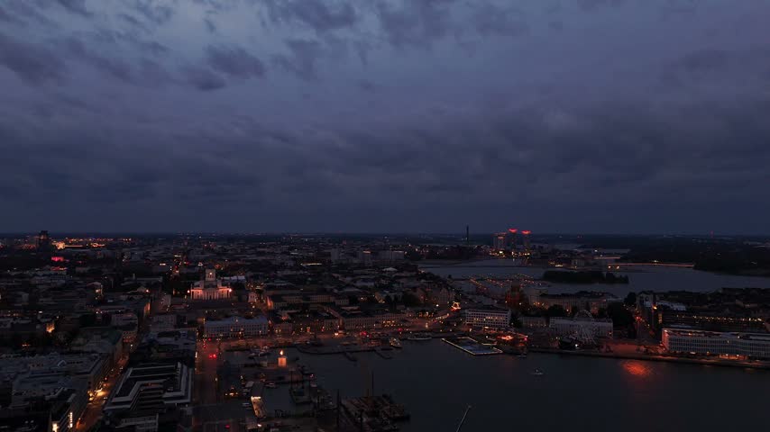 Drone view of Helsinki waterfront at dusk featuring two historic churches the Ferris wheel and illuminated architecture reflected in the evening atmosphere