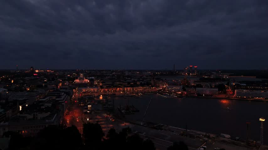Aerial drone shot of Helsinki at dusk showing the central city skyline illuminated streets historic buildings and waterfront areas under a fading blue sky