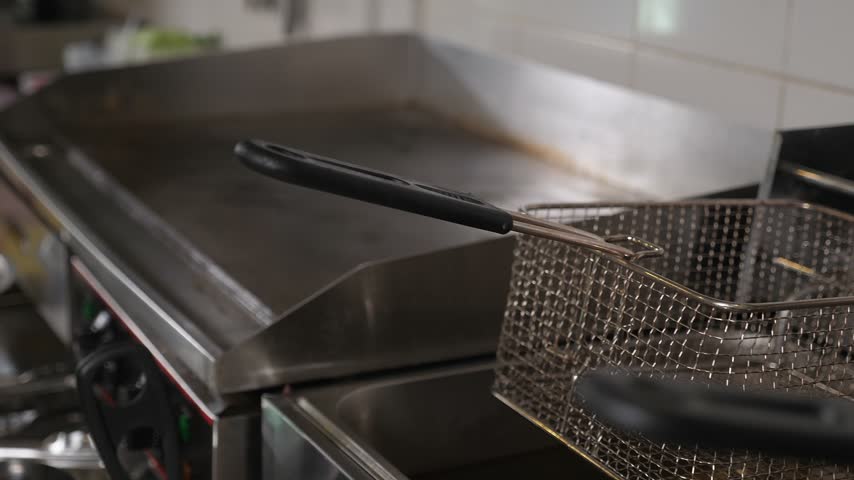 A detailed view of the empty deep fryers in the commercial kitchen of a fast-food establishment. Two empty fryers, one for French fries and the other for chicken nuggets.