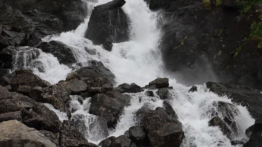 Whitewater rushes over dark rocks in a dramatic Norwegian waterfall surrounded by mist, moss, and rugged wilderness