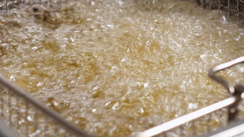 Close-up of deep-fried oil in the kitchen of a restaurant. The process of making various fried snacks in a professional kitchen. Fast food.