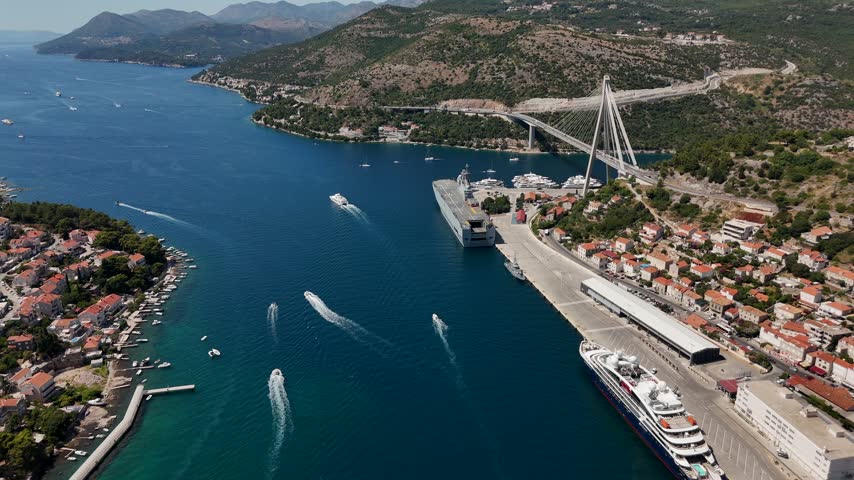 Breathtaking aerial view of Franjo Tudman Bridge and Gruz Port in Dubrovnik Croatia with turquoise sea speedboats cruise ships and a scenic Mediterranean coastline.