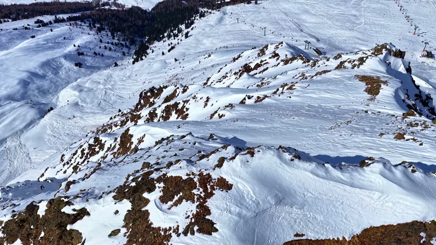Aerial view of snow-covered mountain slopes and rocky terrain with ski lifts in the distance in Schoneben, Oberosterreich, Austria.