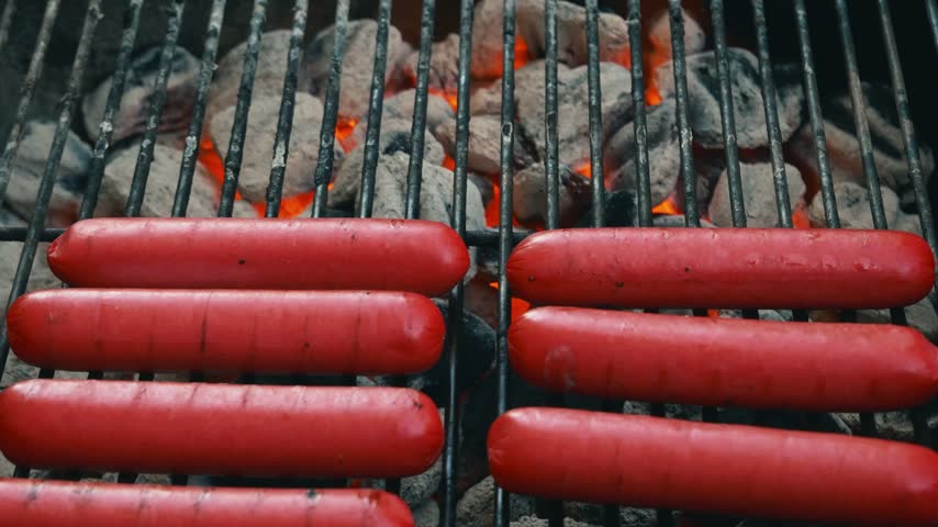 Bright red hot dogs cooking over hot charcoal barbecue coals
