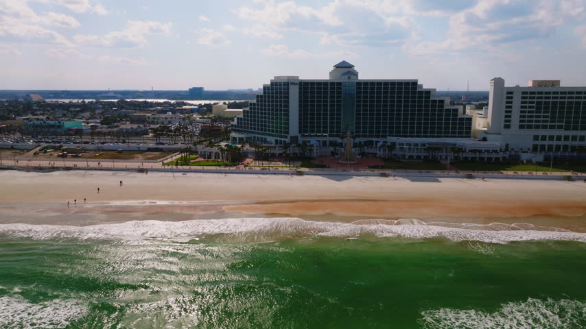 Aerial drone view of beachfront hotels along Daytona Beach, Florida, with Atlantic Ocean waves, sandy shoreline, and coastal cityscape, filmed in ProRes 422HQ