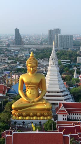 Aerial drone view of giant golden Buddha at Wat Paknam temple with Bangkok skyline in the background. Iconic religious landmark in Thailand.