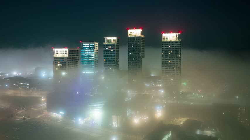 Aerial view of the illuminated Kalasatama towers and REDI shopping mall rising above the night fog in Helsinki, Uusimaa, Finland. Hyperlapse.
