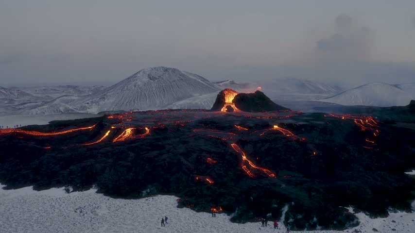 Aerial view of a volcanic eruption with glowing lava flows spreading across a snow-covered landscape in Iceland.