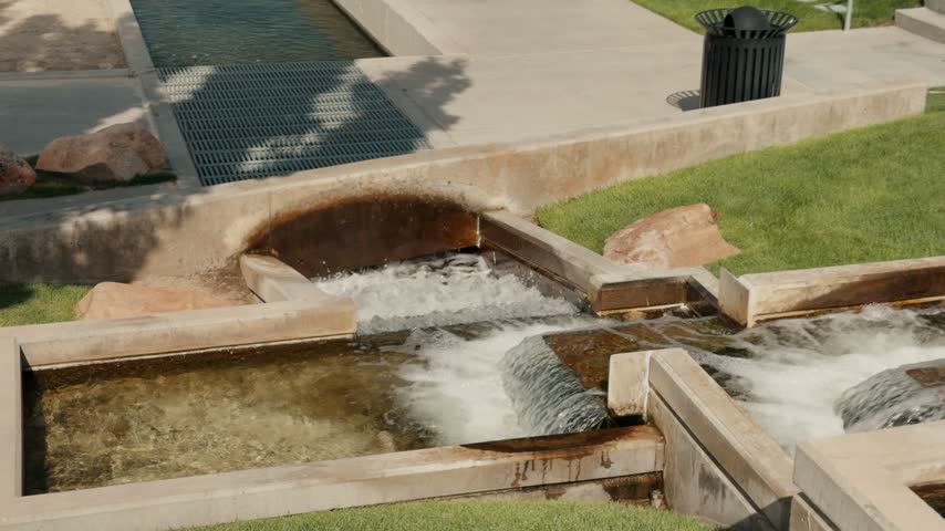 Flowing water fills a geometric concrete fountain beside green grass.