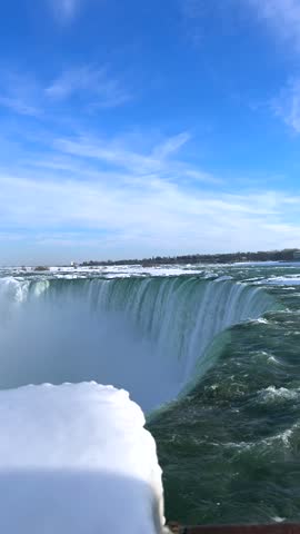 Horseshoe Falls plunges over the edge at Niagara Waterfalls, Canada, with turquoise water, snow-covered ice and rising mist in a vertical winter view
