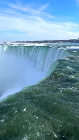 Horseshoe Falls surges over its curved edge in a vertical winter view from the Canadian side, with turquoise rapids, icy cliffs and dense cascading mist