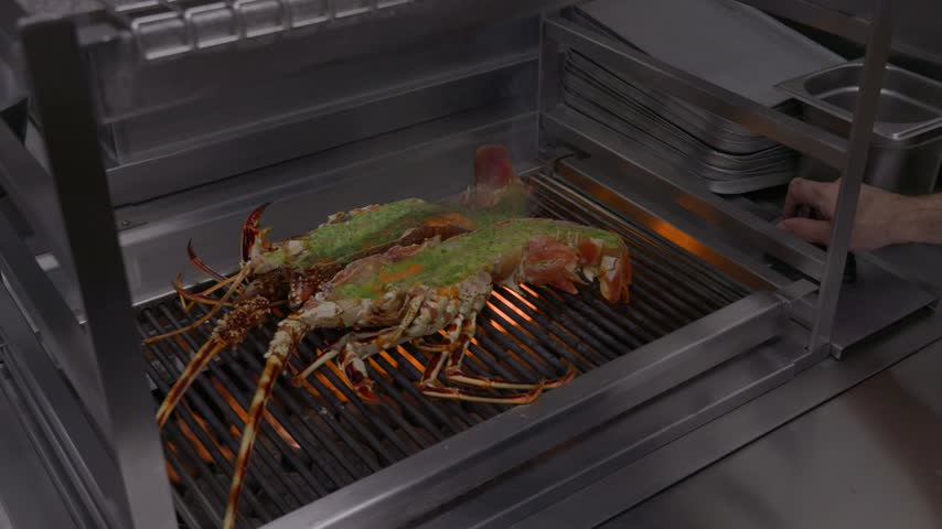 Two split spiny lobsters cook over bright flames on a commercial restaurant grill.