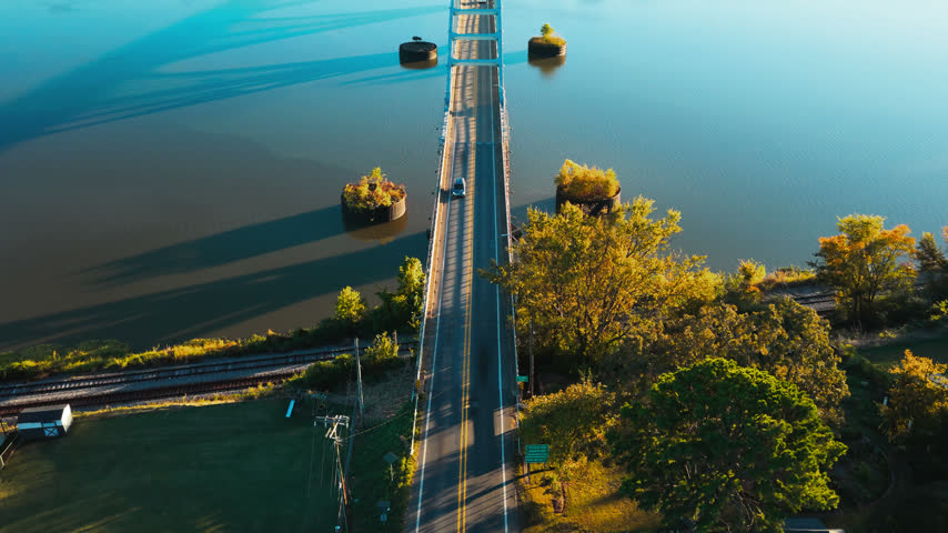 Road bridge crosses calm river beside autumn trees and railroad in Ozark, Arkansas, aerial symmetrical dolly tilts to reveal forested landscape