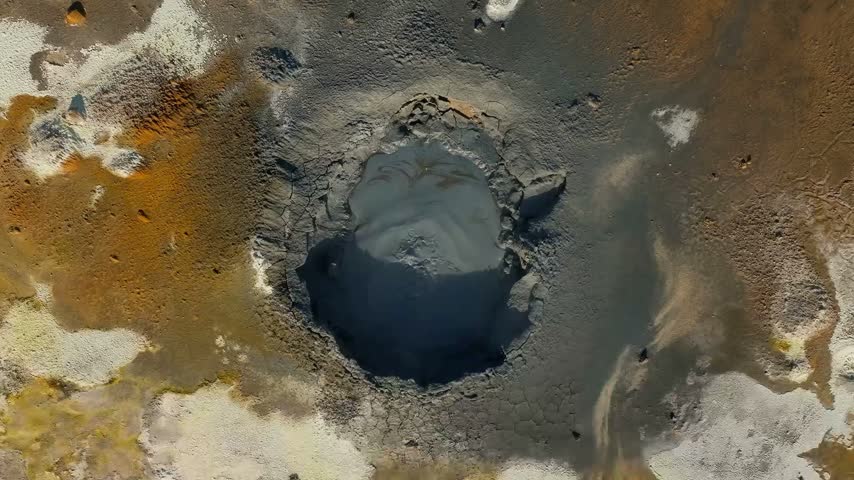 Gray hot bubbling mud pot in a volcanic geothermal area, releasing steam and showing intense geothermal activity, mineral-rich mud, and natural volcanic processes.