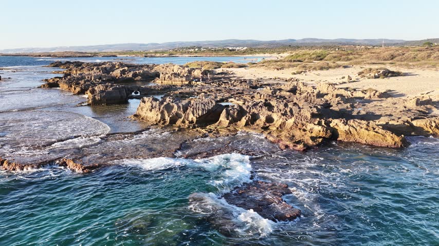Drone shot from the sea of ​​a rocky beach shortly before sunset.