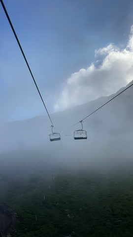 Empty chairlift seats moving through thick fog and clouds in Le Tour near Chamonix Mont Blanc, atmospheric alpine ski lift transport in French Alps, low mist mountain landscape, vertical 9:16 framing