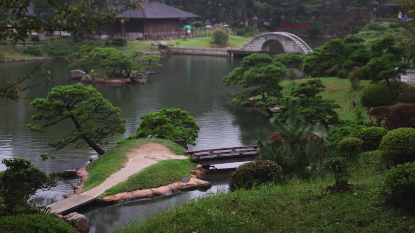 Shukkeien traditional Japanese garden in Naka-ku,  Shukkei-en garden, Hiroshima city, Chugoku region, Japan, with pond and trees, thatched roof teahouse pavilion reflection in a rainy autumn day