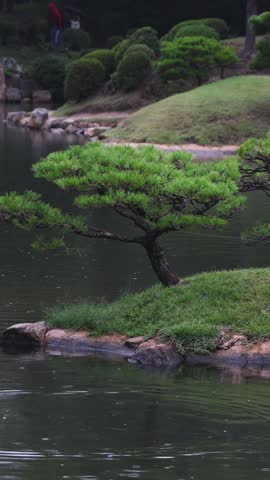 Shukkeien traditional Japanese garden in Naka-ku,  Shukkei-en garden, Hiroshima city, Chugoku region, Japan, with pond and trees, thatched roof teahouse pavilion reflection in a rainy autumn day